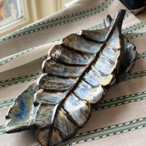 May include: A ceramic leaf-shaped dish with a blue, brown and gold glaze. The dish is made to look like a large leaf.