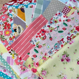 May include: A collection of fabric scraps in various floral patterns, stripes, and colours, including pink, red, yellow, and blue. The fabrics are arranged in a layered stack.
