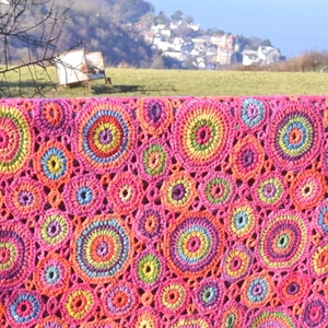 May include: A colorful crocheted blanket with a repeating pattern of multi-colored circles. The blanket is made with a variety of shades of pink, orange, yellow, green, blue, and purple yarn.