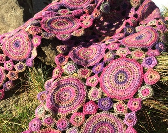 May include: A crocheted shawl featuring a circular pattern in shades of pink, purple, and brown. The shawl is crafted with a variety of different stitches and textures.