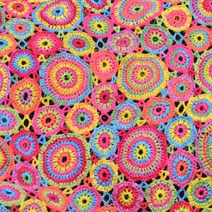 May include: A colorful crocheted blanket with a circular pattern. The blanket is made of multiple colors, including pink, blue, yellow, green, and red.