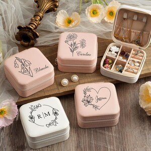 May include: Set of four pink and white jewelry boxes with floral designs and personalized names. The boxes are square and have a hinged lid. Each box has a different floral design and name: Blanche, Caroline, Jessica, and R/M.