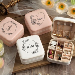 May include: Three pink and white jewelry boxes with floral designs and personalized names. The boxes are open to reveal compartments for rings, earrings, and necklaces.