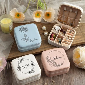 May include: Four square jewelry boxes with floral designs and personalized names. The boxes are in shades of blue, pink, and white. The boxes are open to reveal compartments for storing jewelry.