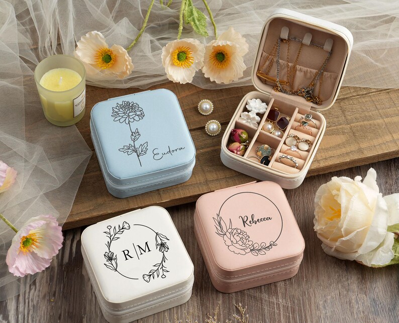 May include: Four square jewelry boxes with floral designs and personalized names. The boxes are in shades of blue, pink, and white. The boxes are open to reveal compartments for storing jewelry.
