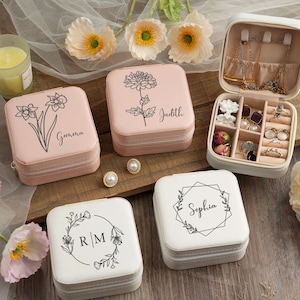 May include: Four pink and white jewelry boxes with different floral designs and names on the lids. The boxes are on a wooden surface with flowers in the background.