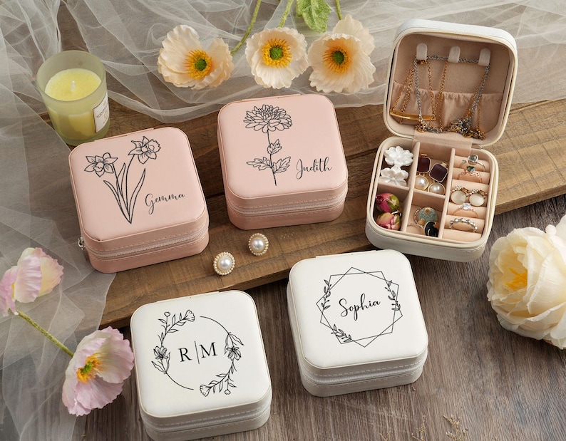 May include: Four pink and white jewelry boxes with different floral designs and names on the lids. The boxes are on a wooden surface with flowers in the background.