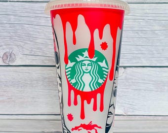 May include: A reusable plastic cold cup with a translucent white finish, featuring a red dripping paint design and the green and white Starbucks siren logo. The cup includes a clear lid and black graphic illustrations of faces on the sides.