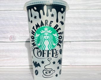 May include: A translucent plastic cold cup with a clear lid, featuring black drip patterns at the top, black stars, bats, and coffee bean graphics. The text reads Nightmare Before Coffee, centered around a green circular siren logo graphic.