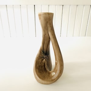 May include: A brown ceramic vase with a unique, twisted design. The vase has a small, dark brown pine cone design on the front.