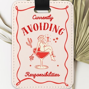 May include: A luggage tag with a cream background and a red border. The tag features the words "Currently Avoiding Responsibilities" and an illustration of a woman in a cocktail glass. A black strap is attached.