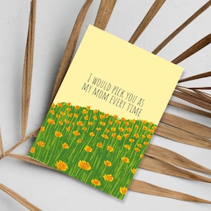May include: A yellow greeting card with the text "I WOULD PICK YOU AS MY MOM EVERY TIME." The card features a green field of grass with orange flowers at the bottom. The card is angled on a light background.