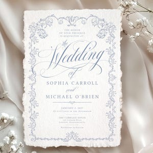 May include: Wedding invitation on textured paper with a light blue floral border and text. The invitation reads "The Wedding of Sophia Carroll and Michael O'Brien" with the date January 2, 2027. The background is a soft, white fabric.