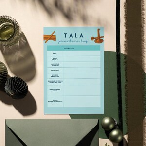 May include: A light blue "TALA practice log" notepad with a teal border, featuring sections for notes. The image includes decorative elements: a glass, two decorative spheres, and an envelope. The notepad is on a light background.