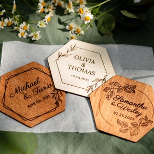 Puede incluir: Tres posavasos de boda de madera con nombres y fechas grabados. Uno es de madera clara con "Olivia & Thomas" y "01.04.2025". Otro es de madera oscura con "Michael & Tania" y "April 6th, 2025". El tercero es de madera clara con "Samantha & Wesley" y "02.25.2025".