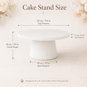 May include: A white cake stand with a fluted base and circular top. Dimensions are 9.4 inches top diameter, 3.9 inches base diameter, 3.9 inches overall height, and 0.6 inches top thickness. Text reads: Cake Stand Size and Designed to fit a 9.8 x 9.8 in 3D printer bed.
