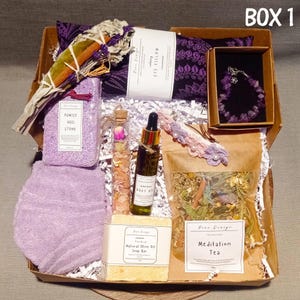 May include: A gift box filled with lavender-themed self-care items, including a lavender eye pillow, a lavender bracelet, a pumice heel stone, a lavender bath towel, a bottle of root oil, a bar of natural olive oil soap, a small glass vial of dried lavender buds, and a bag of meditation tea.