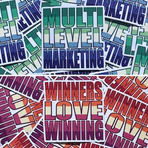 May include: A collection of stickers with bold text. One sticker reads "MULTI LEVEL MARKETING" in green, blue, and white. Another sticker says "WINNERS LOVE WINNING" in shades of red, orange, and purple. The stickers are rectangular with white borders.