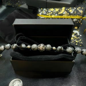 May include: A black velvet-lined box with a silver and black gemstone bracelet. The bracelet has a silver charm with a star and crescent moon design.