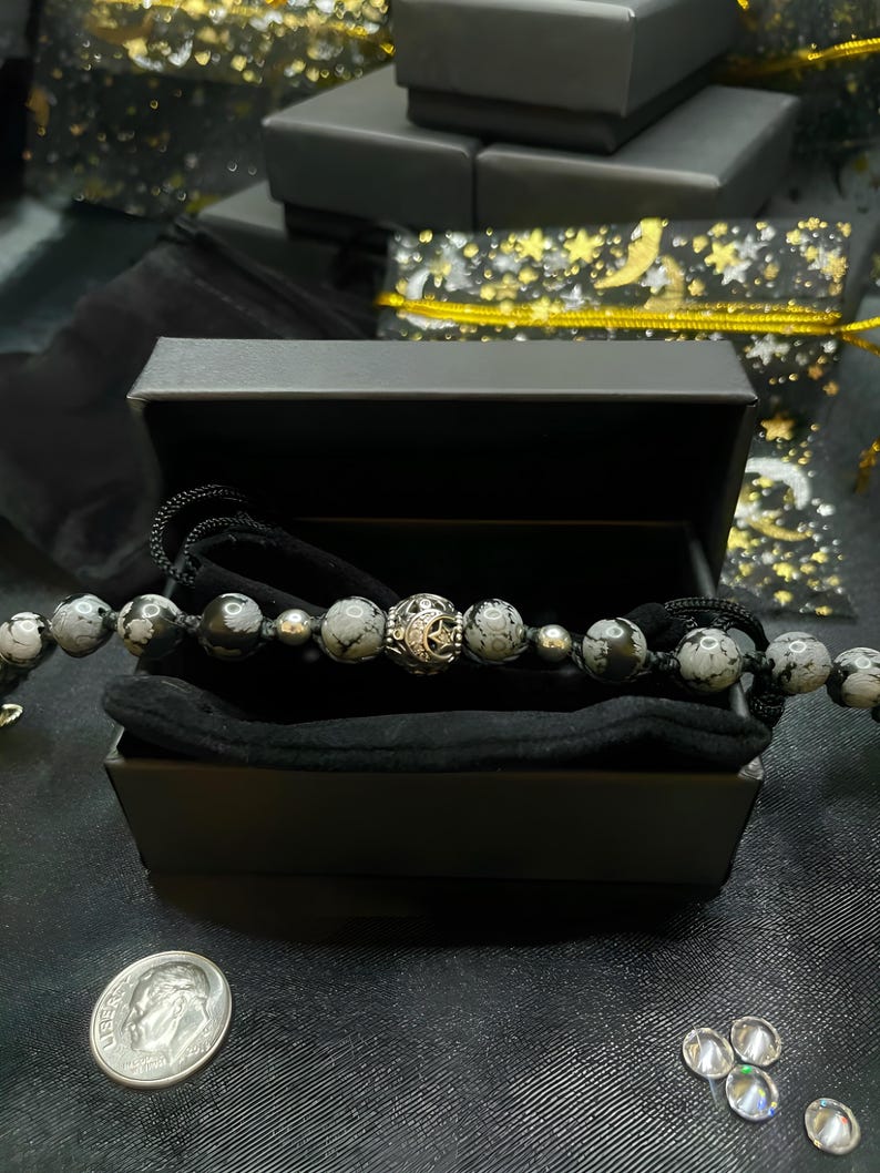 May include: A black velvet-lined box with a silver and black gemstone bracelet. The bracelet has a silver charm with a star and crescent moon design.