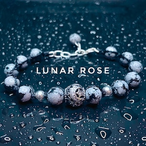 May include: A silver bracelet with a moon and star charm, featuring black and white speckled beads. The bracelet is on a dark blue background with water droplets.