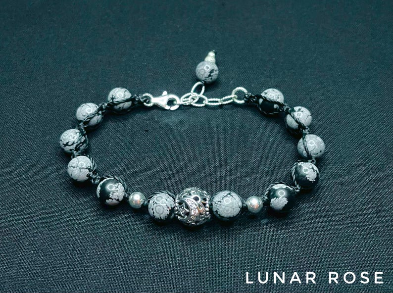 May include: A black and white stone bracelet with a silver clasp and a silver bead in the center. The bracelet is made of round beads with a black and white pattern.