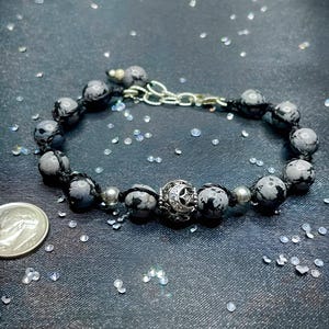 May include: A black and white stone bracelet with a silver charm featuring a crescent moon and star. The bracelet is made with black cord and silver beads.