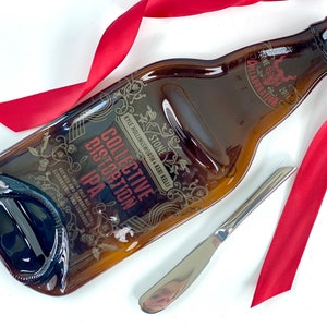 May include: A brown glass bottle shaped serving dish with a gold design and the text "STONE COLLABORATION 2014 STONE KYLE HOLLINGSWORTH KERI KELLI COLLECTIVE DISTORTION IPA INDIA PALE ALE BREWED AND FLAVORED WITH ELDERBERRIES AND CORIANDER".