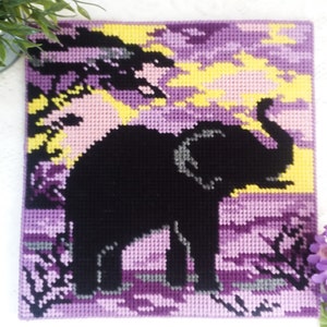 May include: A purple, yellow, and black needlepoint picture of an elephant standing in a field. The elephant is black and the field is a gradient of purple and yellow.