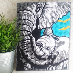 May include: A close-up of a cross-stitch embroidery depicting a white elephant with a blue and yellow eye. The elephant is stitched in shades of gray and white.