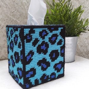 May include: A blue and black leopard print tissue box cover. The cover is made of yarn and is square shaped.