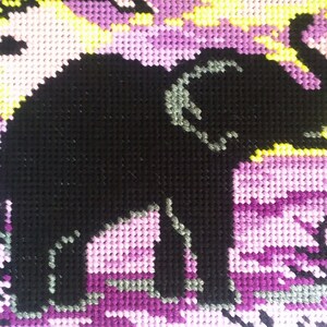 May include: A black and gray elephant silhouette cross-stitched on a purple, pink, and yellow background.