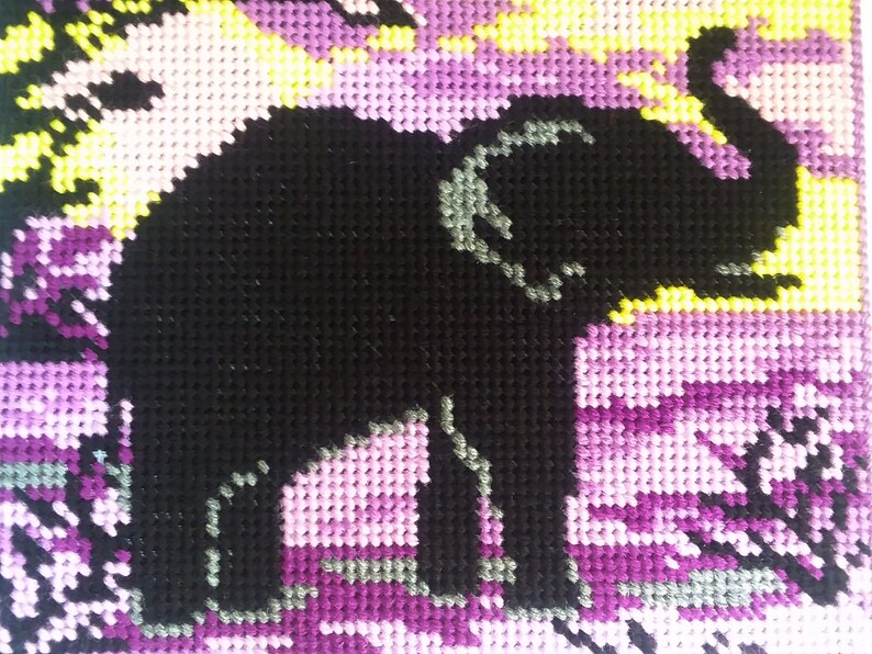 May include: A black and gray elephant silhouette cross-stitched on a purple, pink, and yellow background.