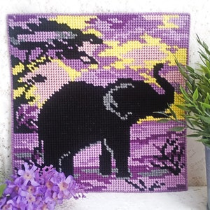May include: A purple, yellow, and black needlepoint picture of an elephant standing in a field. The elephant is a silhouette against a sunset background.