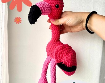 May include: A handmade pink crochet flamingo toy with a black beak and eye. The flamingo is held by a person. The image includes text that says "PDF crochet pattern" and "Domingo the Flamingo".