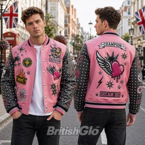 Pode incluir: Uma jaqueta universitária rosa com mangas pretas cravejadas, apresentando vários emblemas bordados, incluindo um coração alado, estrelas e o texto Champion e Dream Big. A jaqueta tem fecho frontal com botões de pressão e acabamento canelado.