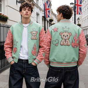 May include: A mint green and pink varsity jacket featuring silver studs on the sleeves. The jacket displays embroidered patches of a teddy bear with an X-shaped eye, a crown, a heart, and flames on both the front and back panels.