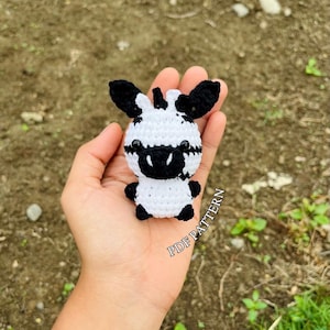 May include: A crocheted zebra amigurumi toy with black and white stripes. The toy is small and is being held in a person's hand. The text "PDF PATTERN" is visible in the image.