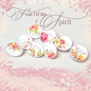 May include: Seven white round buttons with floral designs and the words "Joy", "Peace", "Love", "Prayer", "Faith", "Grace", and "Laughter" on them. The buttons are arranged in a circle on a pink background. The words "Fruit of the Spirit" are written in cursive above the buttons.