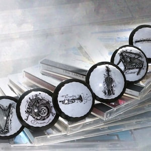 May include: A stack of CDs with black and white illustrations of musical instruments on top. The instruments include a harp, a drum, a trumpet, a violin, a piano, and a flute.