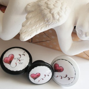 May include: Three round wooden knobs with black and white paint. Each knob features a red heart with a swirl design and the text "You and Me".
