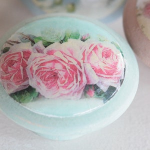 May include: A light blue round knob with a floral design featuring pink roses and green leaves. The knob has a white background and a light blue border.