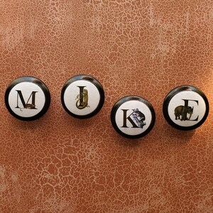 以下が含まれることがあります： 白のセラミックマグカップ、黒いハンドル、手書き風の「But First, Coffee」の文字。マグカップは白い表面に置かれています。マグカップの高さは10cmです。