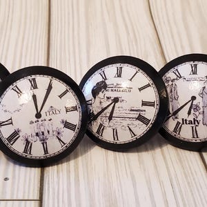 May include: Six black and white clock knobs with different designs. Each knob features a clock face with Roman numerals and a different design in the center. The designs include a clock tower, a woman in a dress, and a scene from Italy. The knobs are all labeled "Italy" or "Clock".