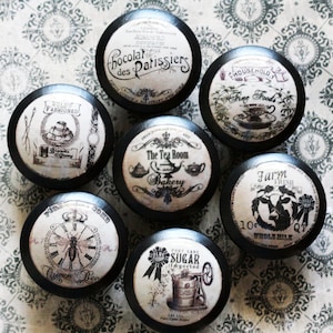 May include: Six black round knobs with vintage-style labels. The labels feature text such as "Chocolar des Patissiers", "The Tea Room and Bakery", "Farm Fresh", "Pure Cane Sugar", "Household Fine Foods", and "Wold Fashioned".