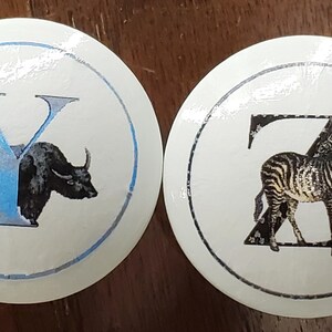 May include: Two white, round cabinet knobs. One features a blue "Y" with a yak illustration, the other a black "Z" with a zebra illustration. Both have a blue and black border.