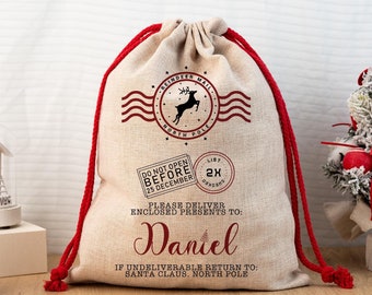 Può includere: Un sacco regalo natalizio beige con coulisse rossa. La borsa presenta un timbro postale con renna, il nome "Daniel" e il testo "Do Not Open Before 25 December". Progettato per la consegna di regali.