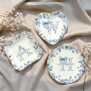 May include: Three decorative plates in various shapes: square, heart, and round. Each plate is white with a blue floral design and a gold rim. The plates feature names: Amelia, Wendy, and Helene.
