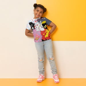 May include: A young person wearing a colourful t-shirt with a graphic print of people and a splash of paint. They are wearing blue jeans with distressed knees and pink trainers.