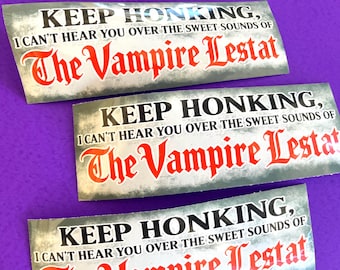 May include: Three rectangular bumper stickers with a distressed grey background. The text reads: KEEP HONKING, I CAN'T HEAR YOU OVER THE SWEET SOUNDS OF The Vampire Lestat. The words are printed in black and bold red gothic-style lettering.